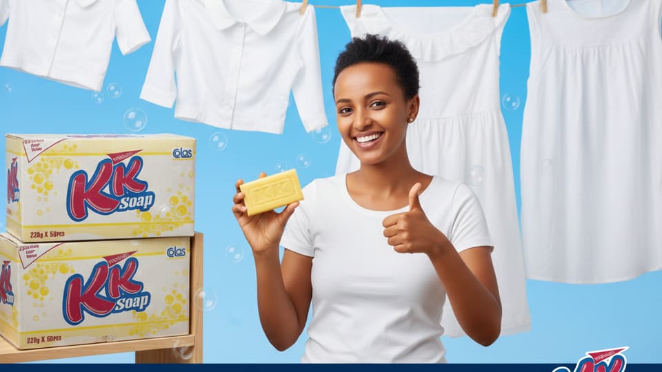 A woman holding a KK bar beside stacked cartons, with bright white washing drying behind.